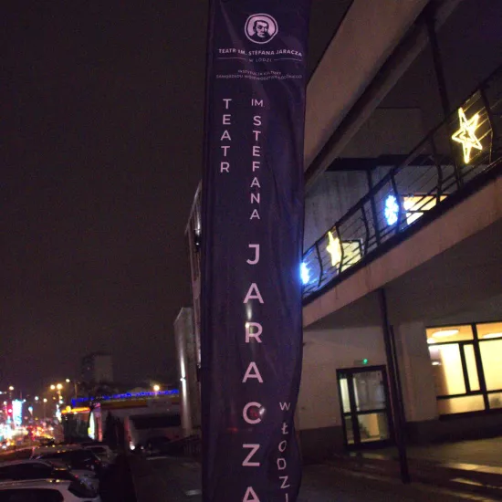 zdjęcie przedstawia flagi Teatru Jaracza w Łodzi z napisem z nazwa instytucji. Flagi są duże, umieszczone na stelarzach przed wejściem do budynku MDK w Radomsku. 