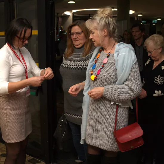 zdjęcie przedstawia grupę osób oczekujących na sprawdzenie biletów przed wejściem na salę teatralną