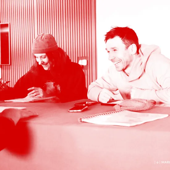 Zdjęcie przedstawia pierwszą próbę spektaklu „Morderstwo w hotelu". Po lewej stronie stołu siedzi aktor Mariusz Witkowski. Na przeciwko niego, po drugiej stronie stołu siedzą aktorzy Natalia Klepacka i Krzysztof Wach. Aktorka ma na głowie czapkę. Wszyscy aktorzy się śmieją. Na zdjęcie został nałożony czerwony filtr.